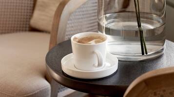 A clear glass vase with a plant on a table next to a cup of coffee.