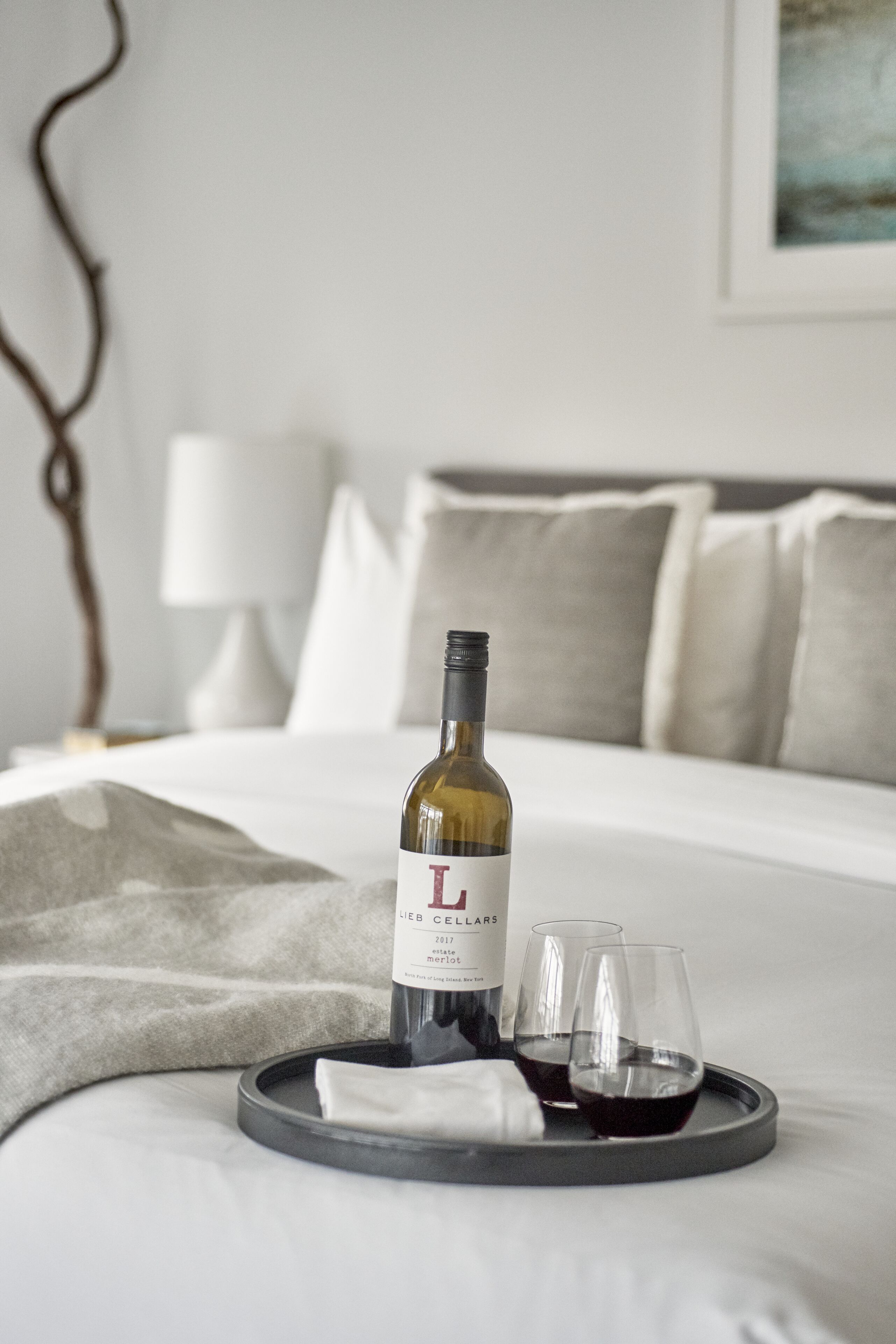 Un lit avec une bouteille de vin et deux verres sur un plateau.