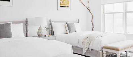 A bedroom with two beds, a bench, a nightstand with a lamp, and artwork on the walls.