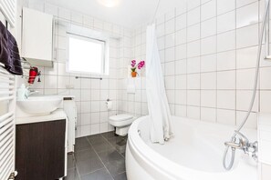 A modern bathroom with a bathtub, toilet, and sink. - Tripcologne Apartments since 2013 (Cologne)