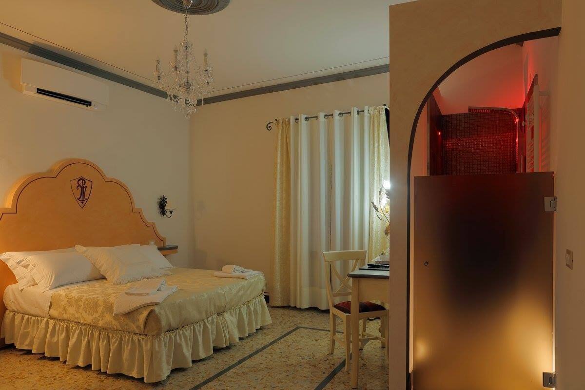 Hotelkamer met een bed, bureau, stoel, een kroonluchter en een deur met een rood licht.