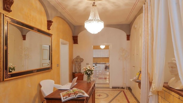 A hallway with a wooden desk, a large mirror, and a chandelier. - Palazzo Mari Suite & Rooms (Montevarchi)