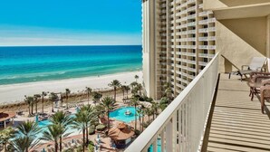 A high-rise hotel with a balcony overlooking a beach and a pool area.