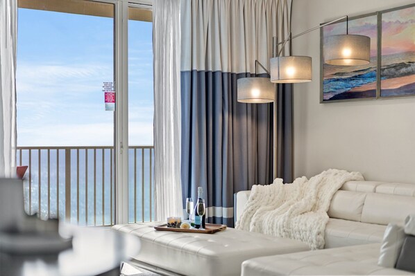 Een moderne hotelkamer met balkon, een witte bank, een zachte plaid en een schilderij van een strand.
