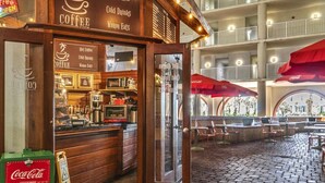 A coffee shop with a wooden facade, a Coca-Cola cooler, and outdoor seating with red umbrellas.