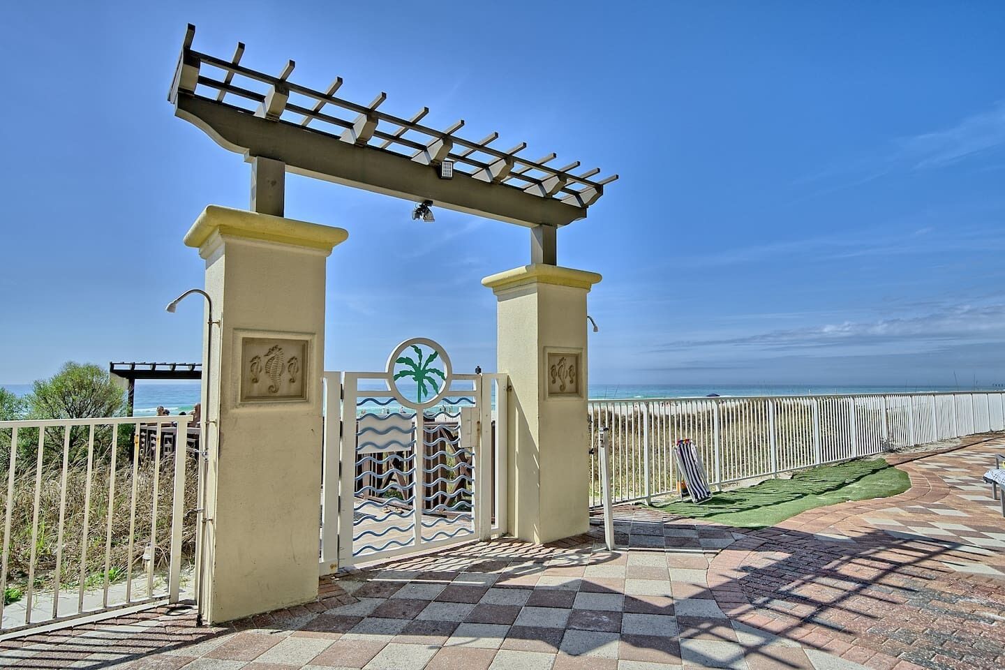 A gated entrance with a pergola overhead, a palm tree symbol, and a view of the sea.