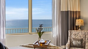 A room with a large window overlooking the sea, a patterned armchair, and a table with a tray.