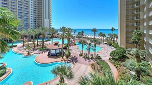 A resort with a large swimming pool, palm trees, and a view of the ocean.