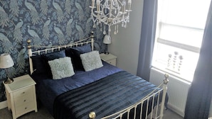 A bedroom with a bed, nightstands, a chandelier, and a window with curtains. - Lion House Bed and Breakfast (Ilfracombe)