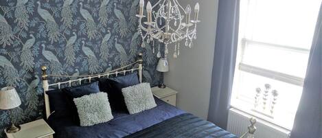 A bedroom with a bed, nightstands, a chandelier, and a window with curtains.