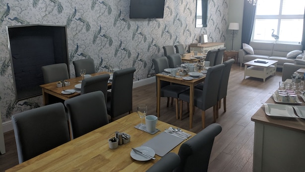A dining area with a wooden table set for six, surrounded by chairs. A flat-screen TV is mounted on the wall above the table. - Lion House Bed and Breakfast (Ilfracombe)