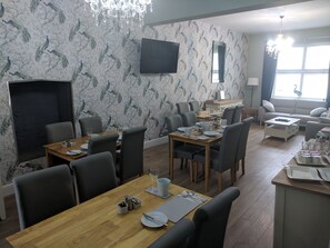 A dining area with a wooden table set for six, surrounded by chairs. A flat-screen TV is mounted on the wall above the table. - Lion House Bed and Breakfast (Ilfracombe)
