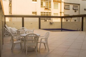 A courtyard with a pool, white plastic chairs, and tables. - Atlântico Golden Apart Hotel (Santos)