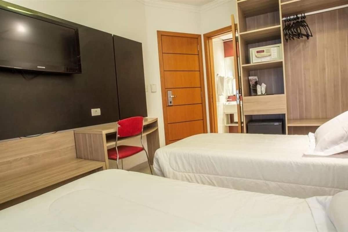 Habitación de hotel con dos camas, televisión, escritorio y armario.
