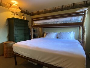 Un dormitorio con una cama litera, un aparador verde, una lámpara y una cesta de mimbre.