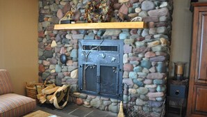 A stone fireplace with a metal door, a wooden shelf above it, and a woven basket with logs beside it. - Mountain Harbor #137 3 Bedroom Condo (Whitefish)