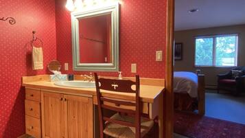 A bathroom with a wooden vanity, a large mirror with lights, and a red polka dot wall.