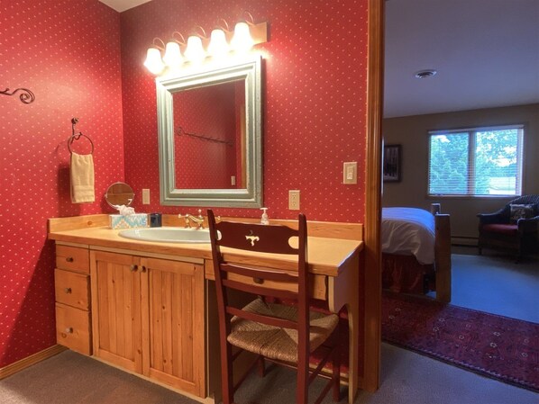 Un baño con tocador de madera, un espejo grande con iluminación y una pared con lunares rojos.