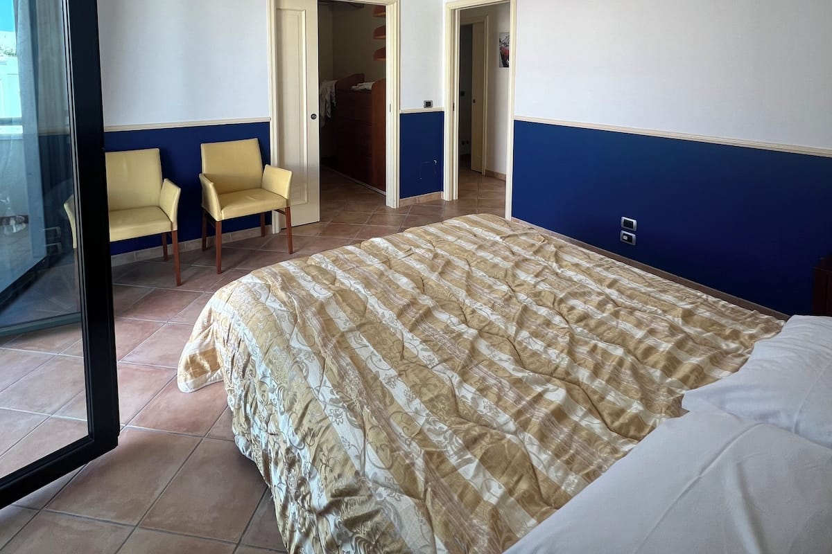 A hotel room with a bed, two chairs, a door leading to another room, and a window.