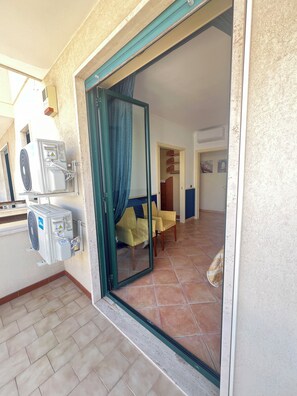 A room with a sliding glass door leading to a balcony, a ceiling fan, and a tiled floor.