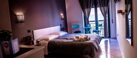 A hotel room with a large bed, a small table, a chair, and a balcony with a view.
