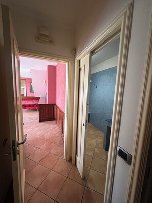 A corridor with tiled flooring leading to a room with a blue tiled wall and a door with a handle.