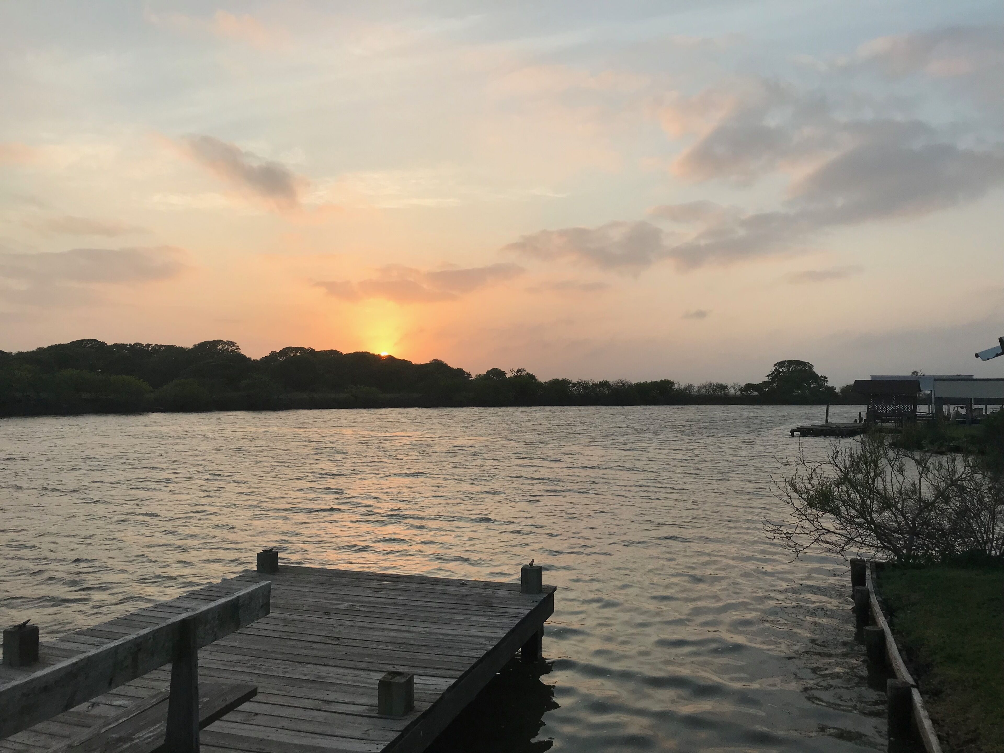 A wooden dock extending into calm water with a sunset in the background.