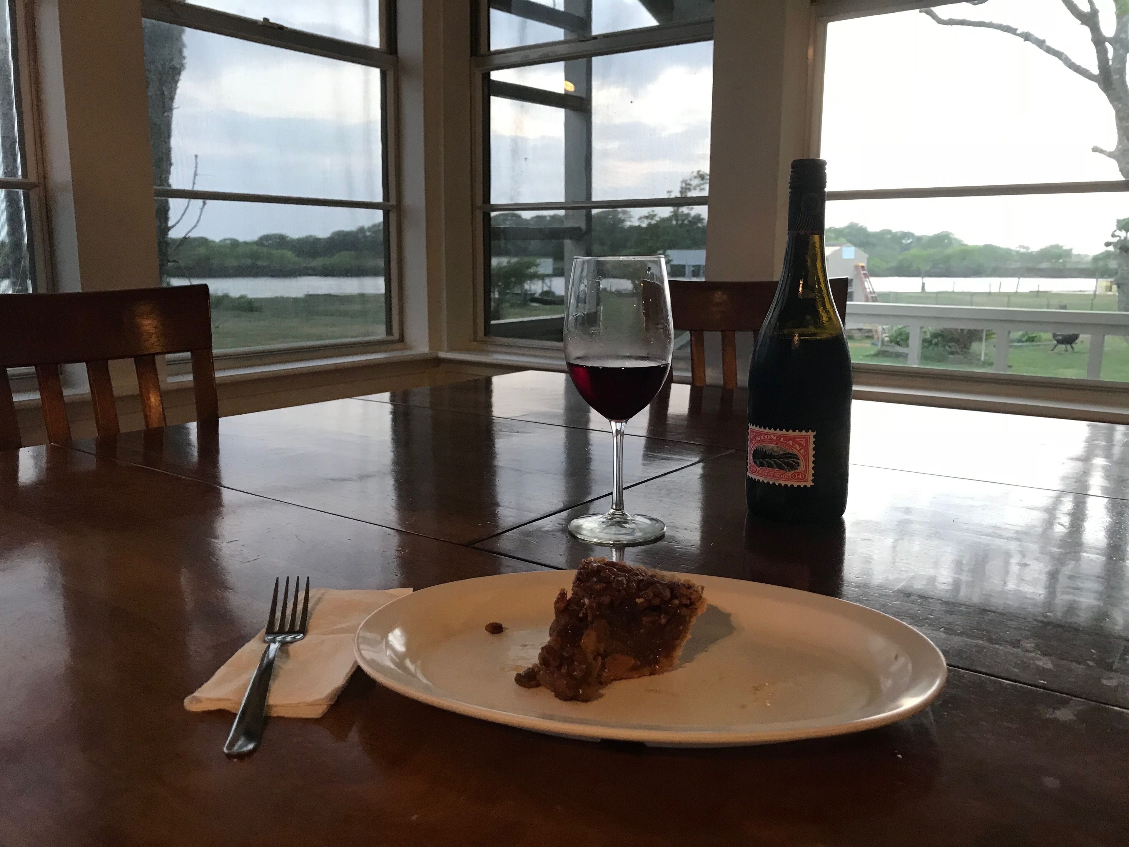 A dining table with a plate of pie, a glass of red wine, and a bottle of wine.