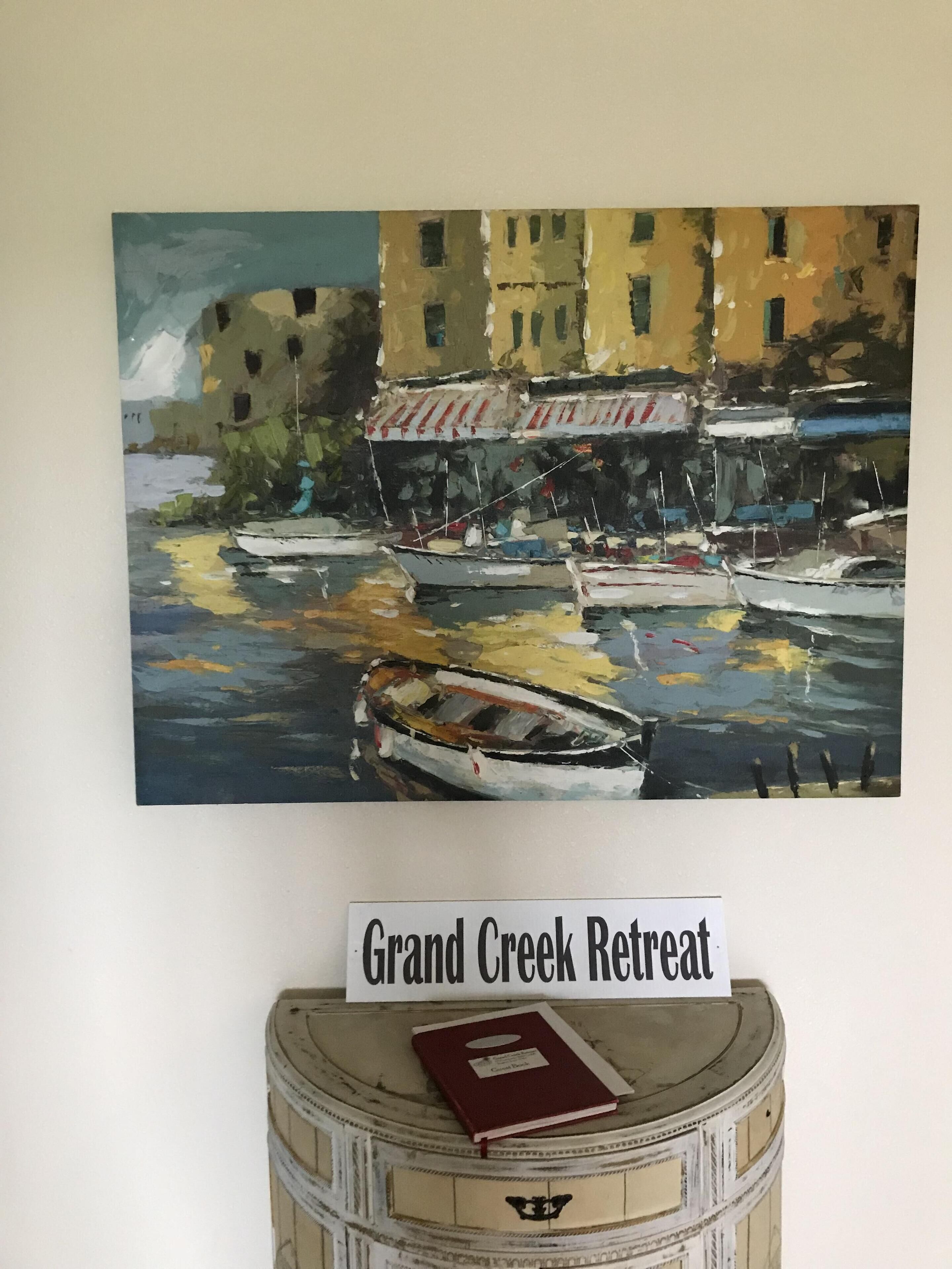 Dipinto di barche sull'acqua con edifici sullo sfondo, un cartello con la scritta 'Grand Creek Retreat' sopra una botte con un libro sopra.