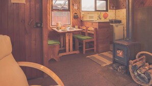 A cozy kitchen with wooden walls, a stove, and a dining area with chairs and a table. - Silvestre Cabanas (Puerto Varas)