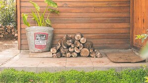 A wooden exterior wall with a metal door, a potted plant, and a stack of firewood. - Silvestre Cabanas (Puerto Varas)