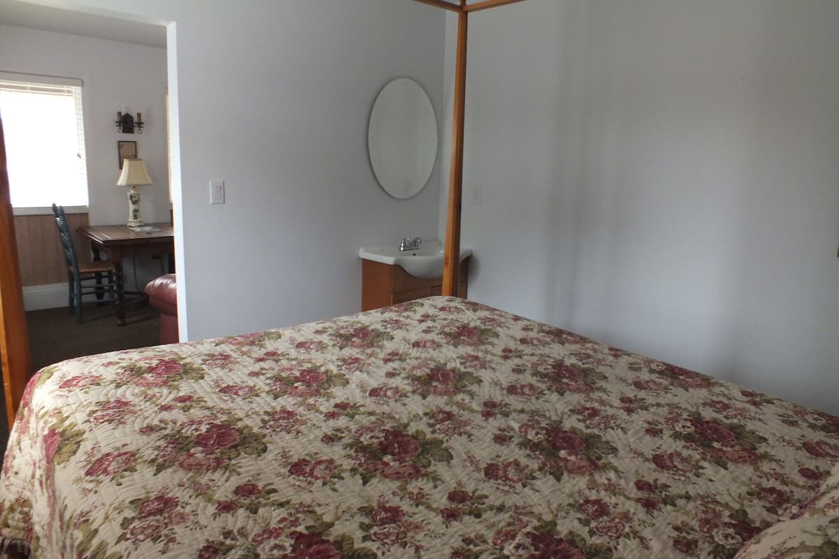 A bedroom with a four-poster bed, a desk with a lamp, and a chair.