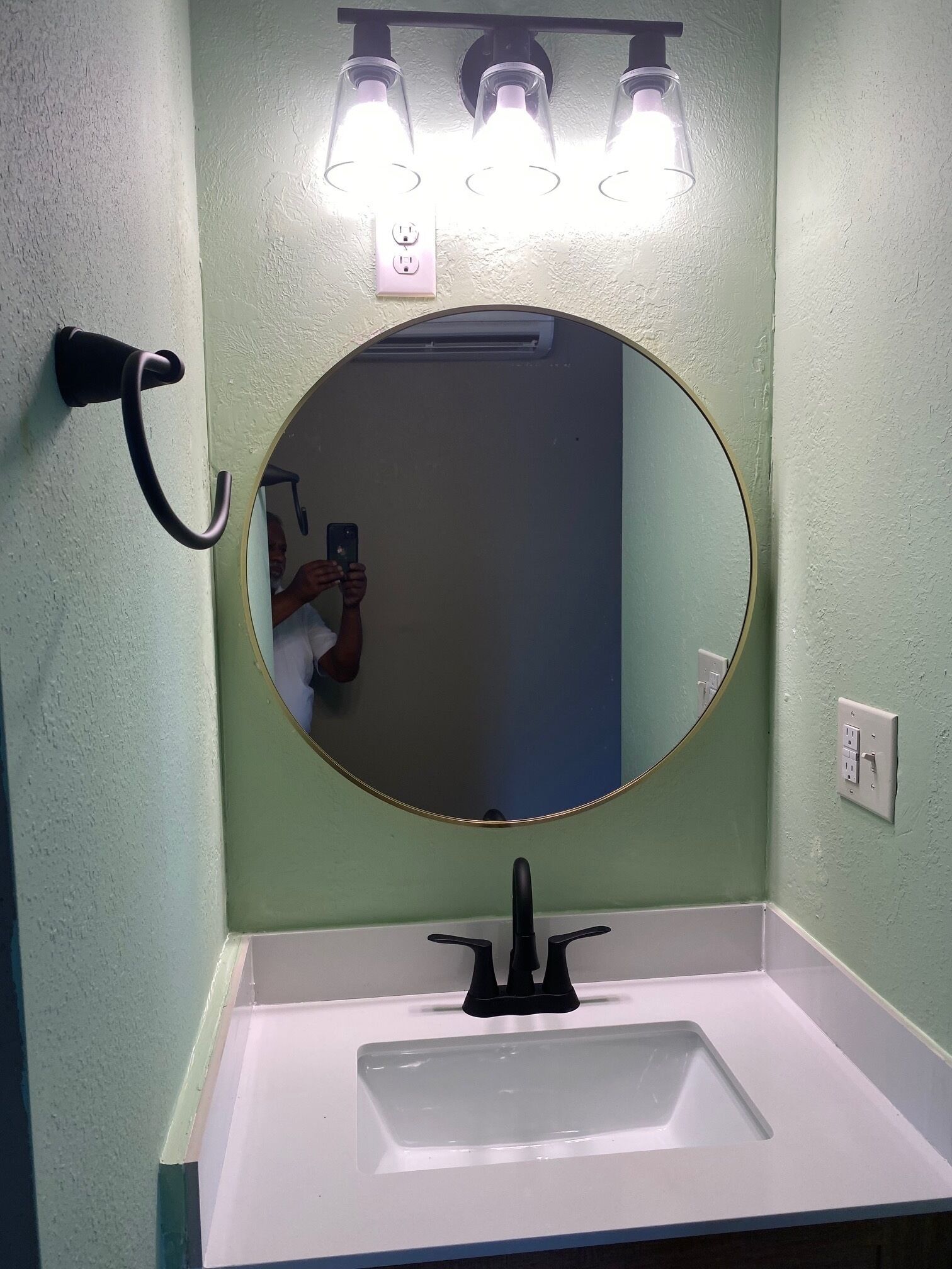 A bathroom with a round mirror, a white sink, and three wall-mounted lights.