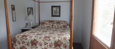 A four-poster bed with floral bedding, a bedside table with a lamp, and framed pictures on the walls.