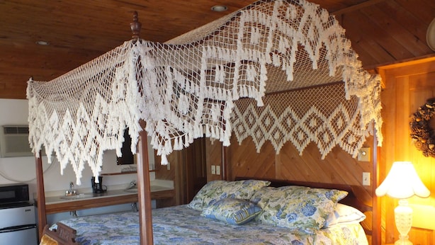 A four-poster bed with a floral bedspread, a wooden headboard, and a nightstand with a lamp.