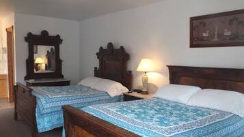 Habitación de hotel con dos camas individuales, cabeceros de madera, una mesita de noche con lámpara, un espejo y un cuadro en la pared.
