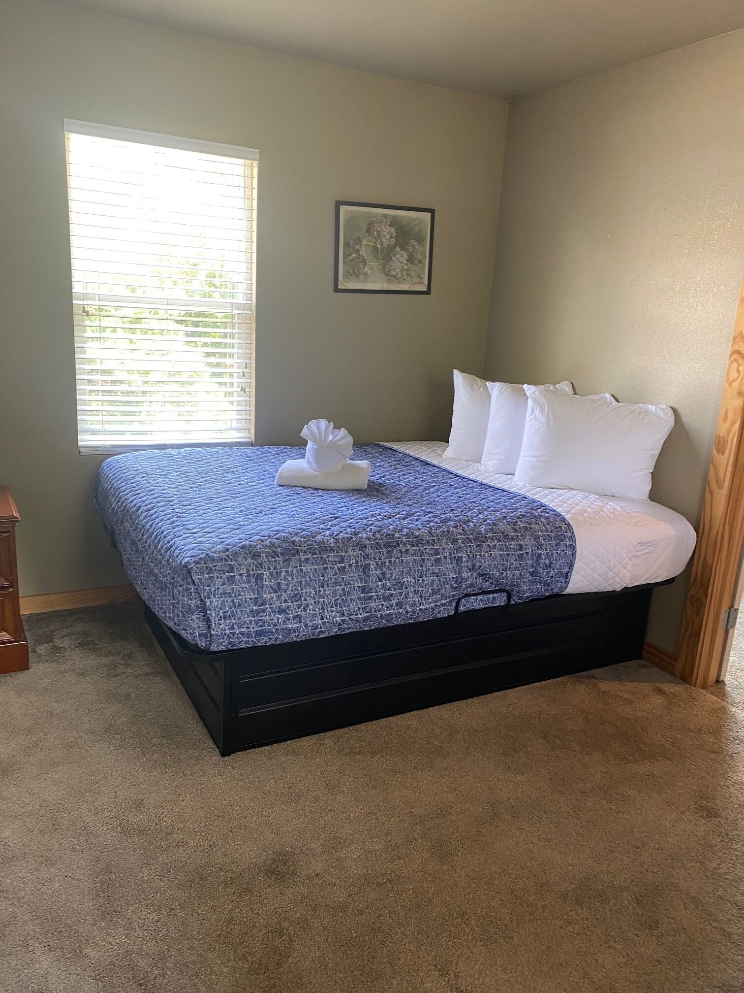 A bedroom with a bed, a window, a picture on the wall, and a wooden door.