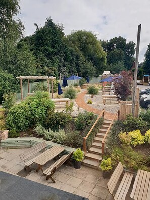A garden patio with wooden benches, a wooden pergola, and a gravel path. - The Red Lion (Rugby)