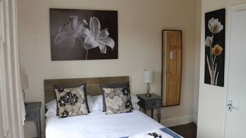 A neatly made bed with floral-patterned pillows, a bedside table with a lamp, and a door to the right.