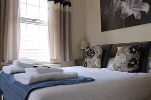 Una cama bien hecha con toallas, un plaid azul y almohadas estampadas con motivos florales.