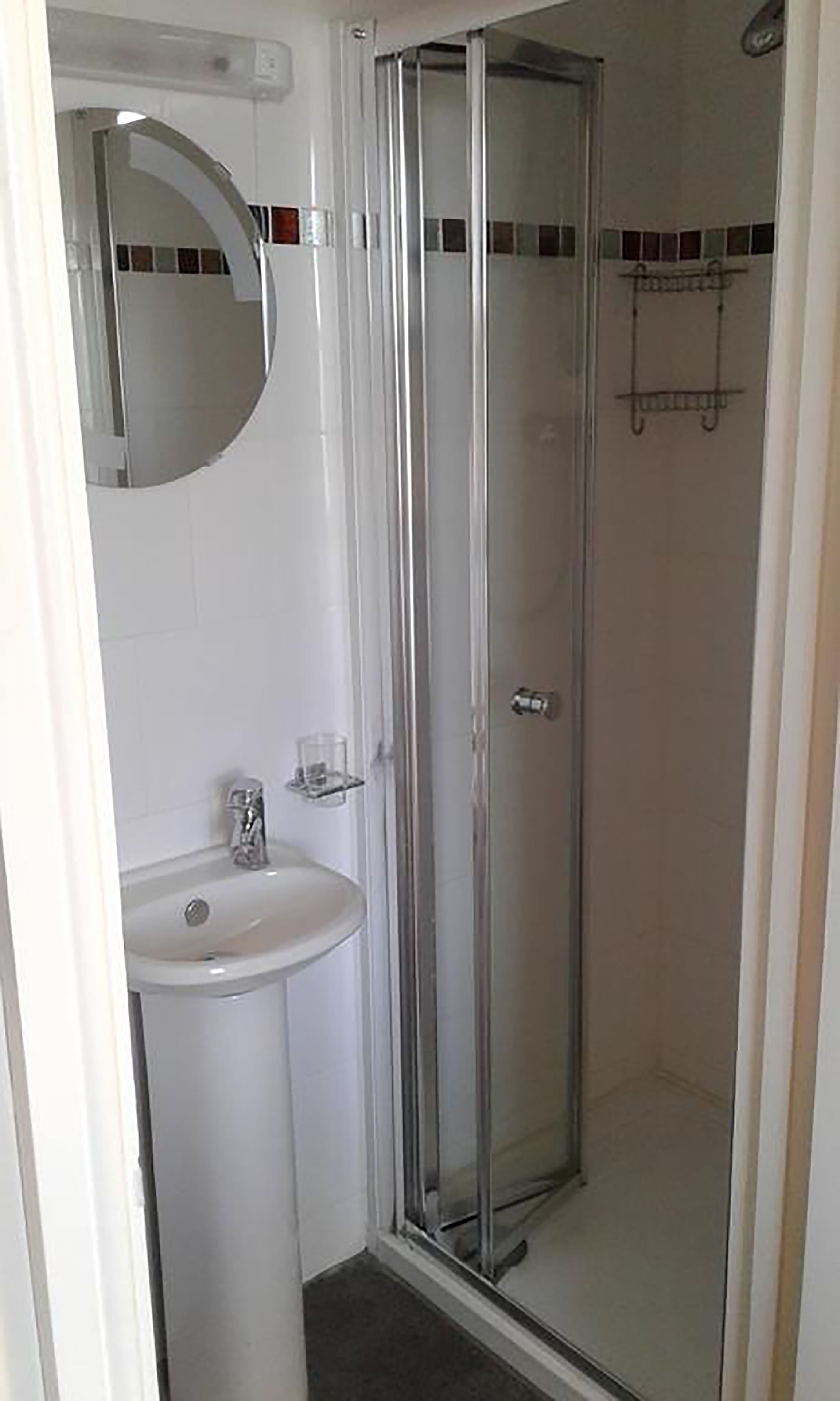 Un baño con cabina de ducha de vidrio, un lavabo blanco y un espejo.