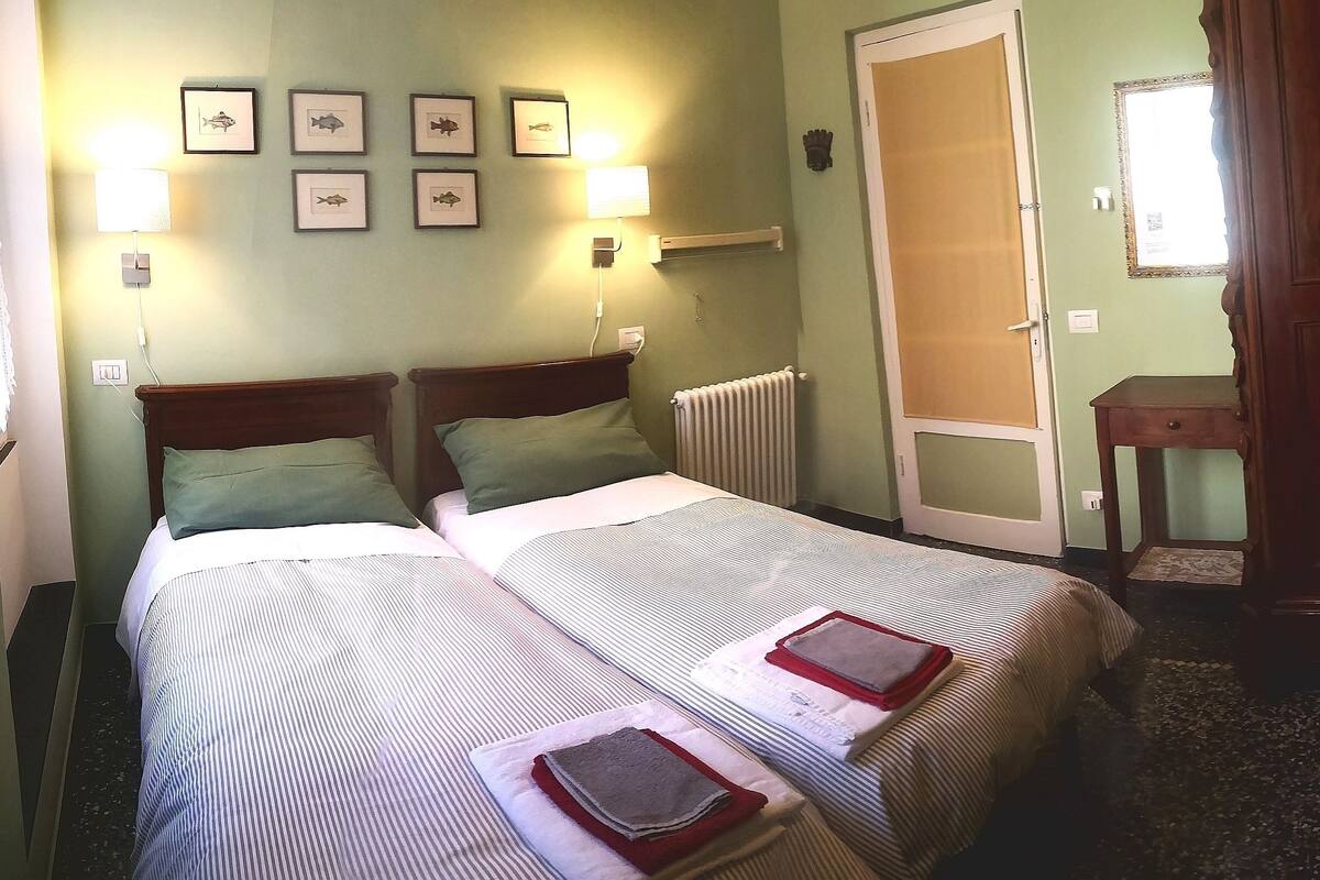 A hotel room with two beds, a radiator, framed pictures on the wall, and a wooden door.