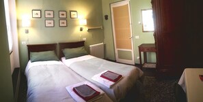 A hotel room with two beds, a radiator, framed pictures on the wall, and a wooden door. - B&B Lavagna Uno (Genoa)