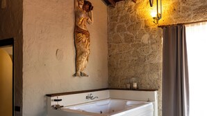 A bathroom with a large bathtub, a stone wall, and a wooden ceiling.
