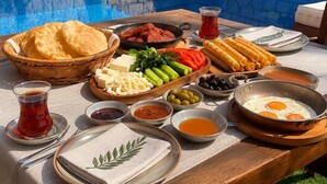 A table with a variety of foods and drinks, a pool in the background, and a stone wall with greenery.
