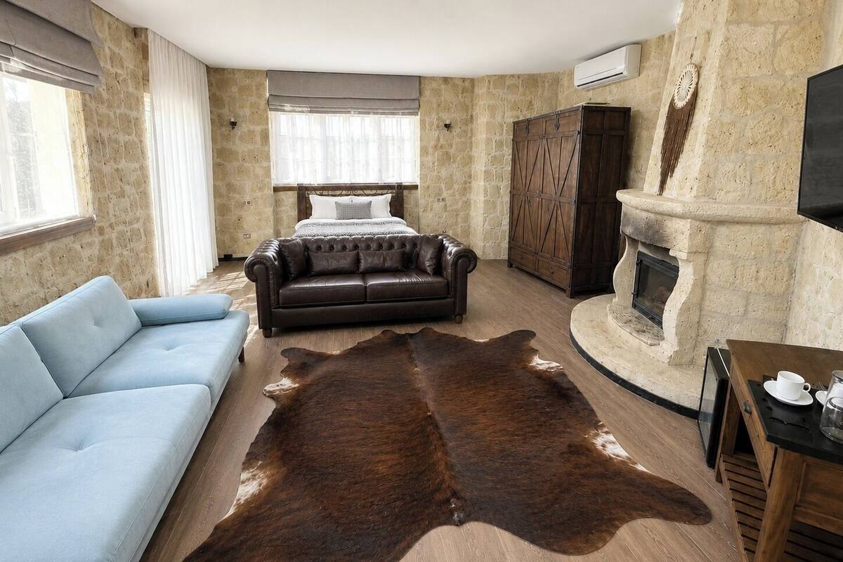 Ein Zimmer mit Steinwand, Ledersofa, blauem Schlafsofa, großem braunen Teppich, einem Bett, einem Holzschrank und einem Kamin.