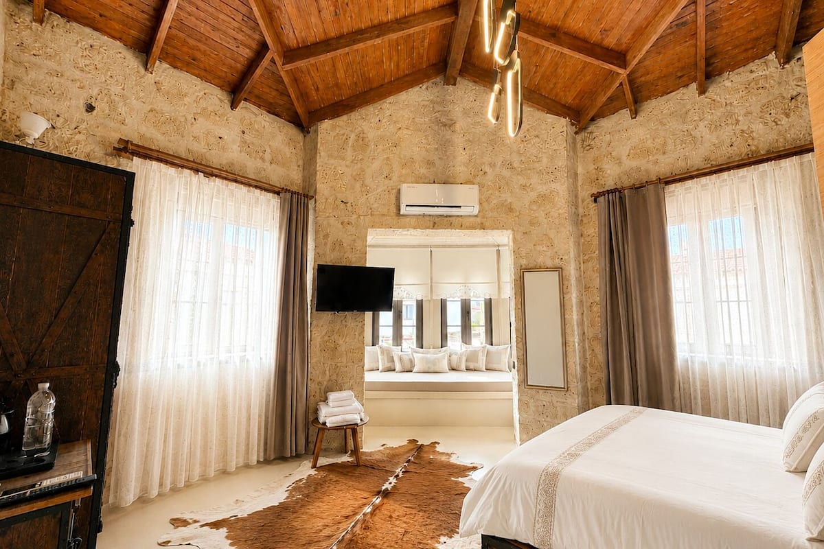 Ein Schlafzimmer mit Holzbalkendecke, einem großen Spiegel, einem Flachbildfernseher, einem Bett und einem Kuhfellteppich.