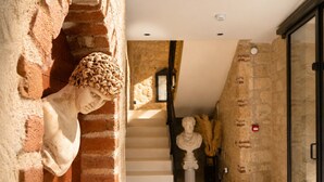 A marble bust against a brick wall, a staircase with white steps, and a classical statue in the background.