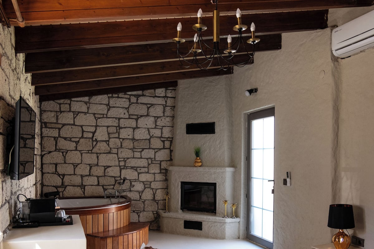 Ein Schlafzimmer mit Steinwand, Kamin, einem großen Bett, einer Holzbadewanne und einer Decke mit freiliegenden Balken.