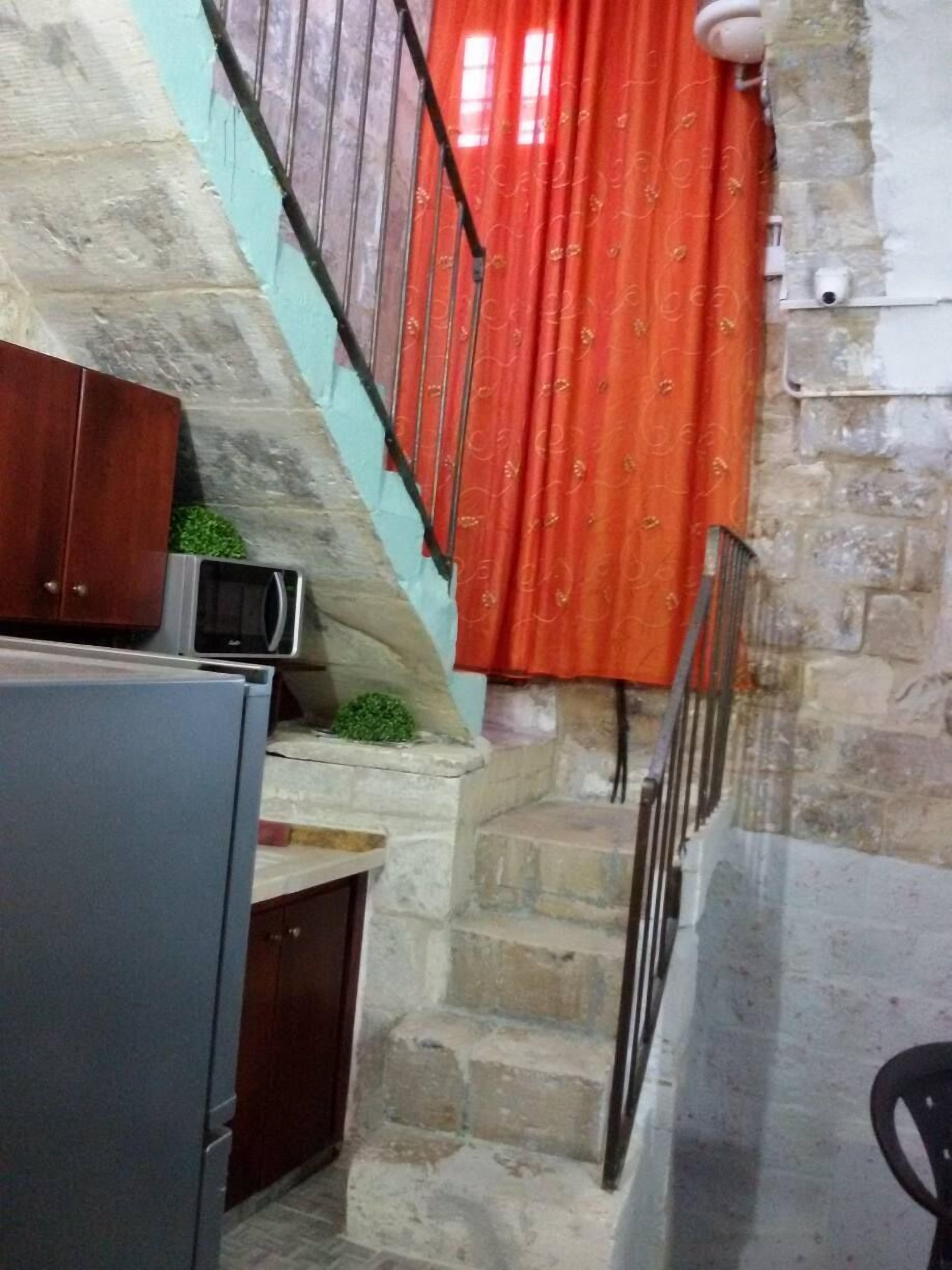 A kitchen with a microwave, a refrigerator, and a staircase leading to a room with a red curtain.